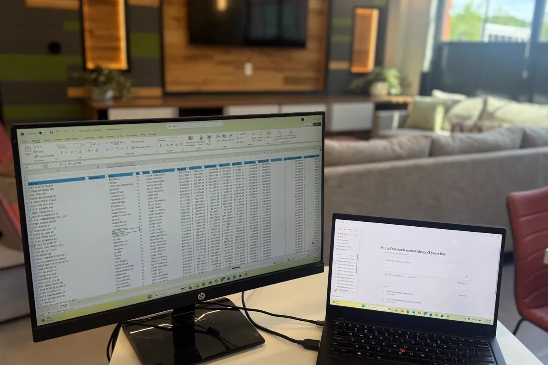 Two screens on a desk, a spreadsheet of loan records open for review.